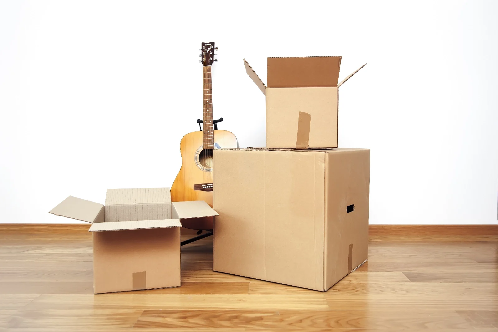 Guitar next to cardboard boxes on wooden floor.