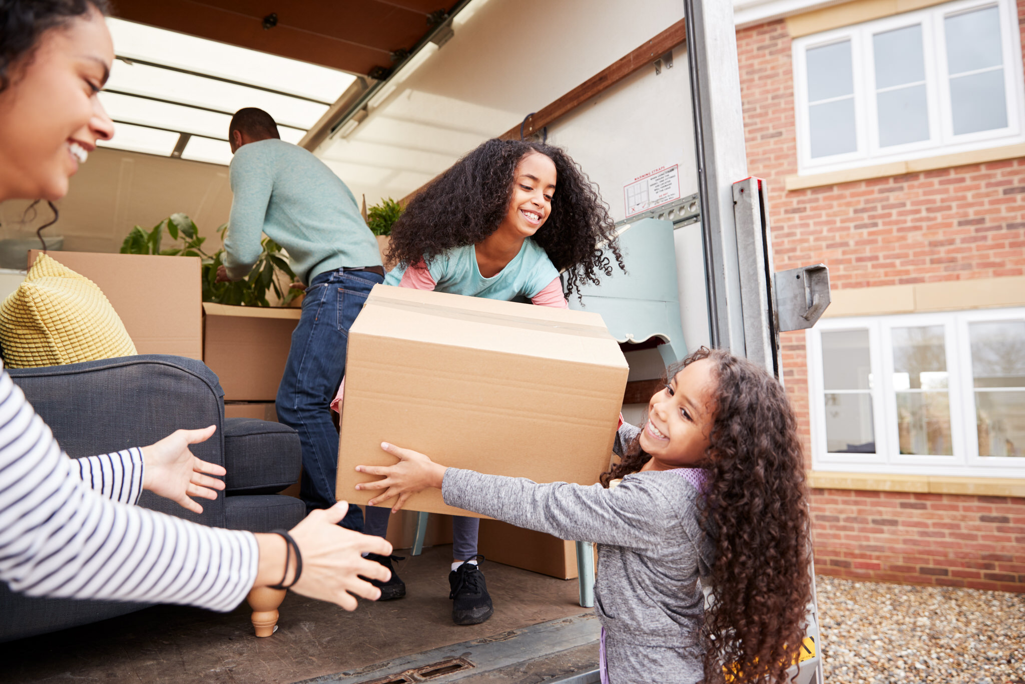 Smiling family moving boxes from van to home.