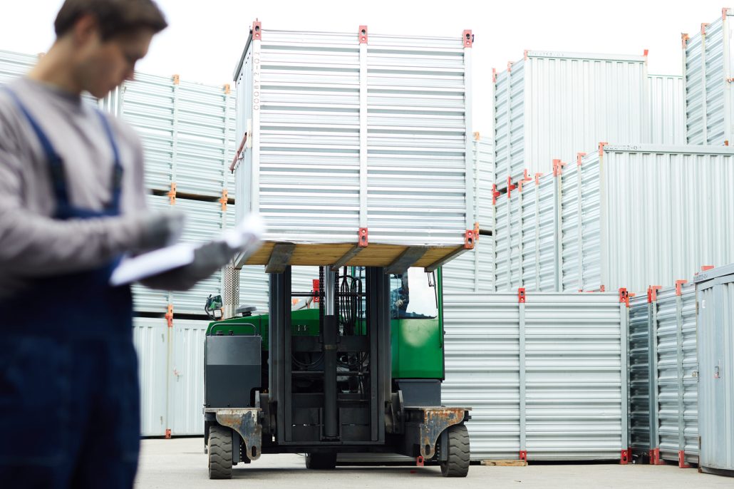 Forklift transporting containers in storage area.