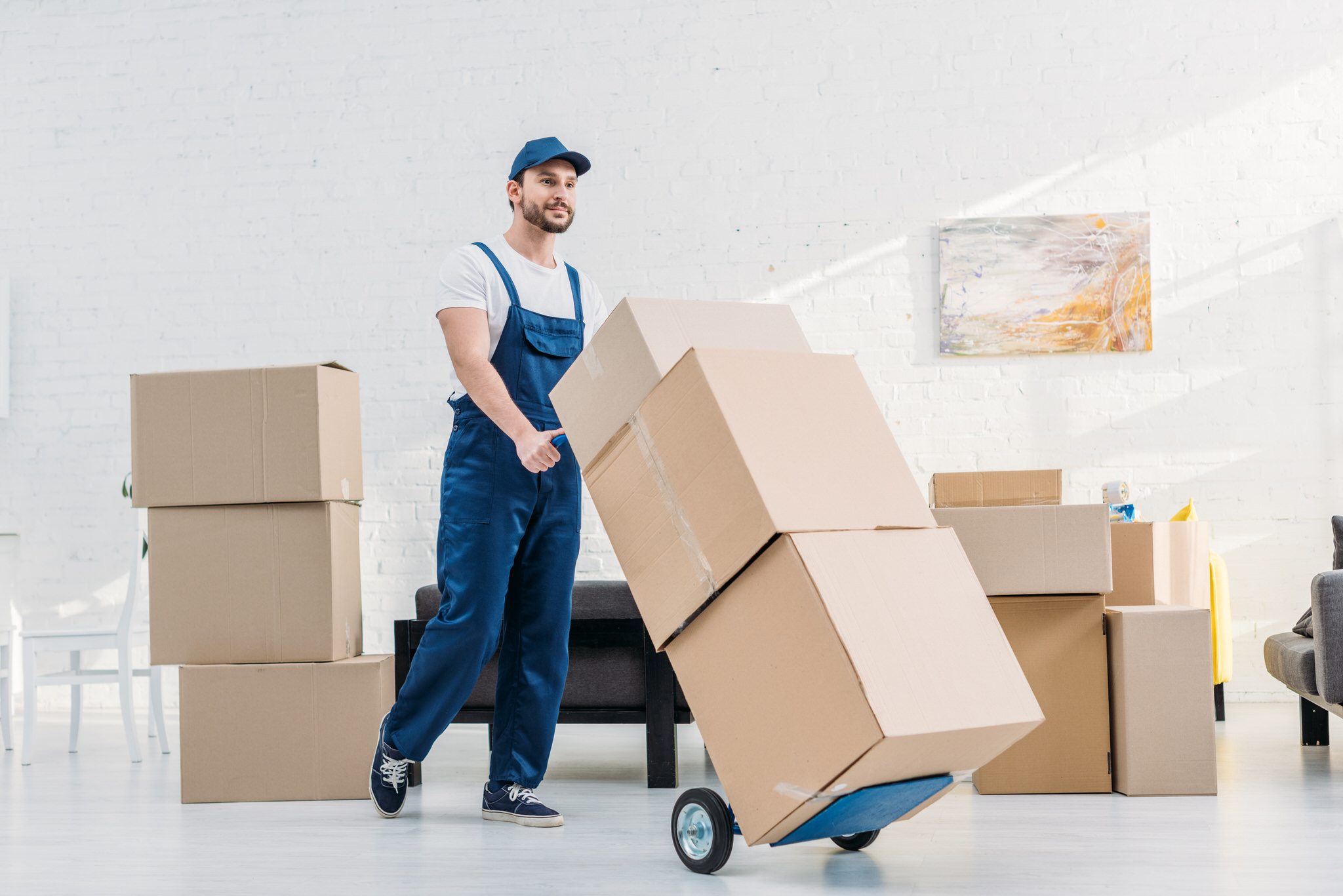 Man moving cardboard boxes with a trolley indoors.
